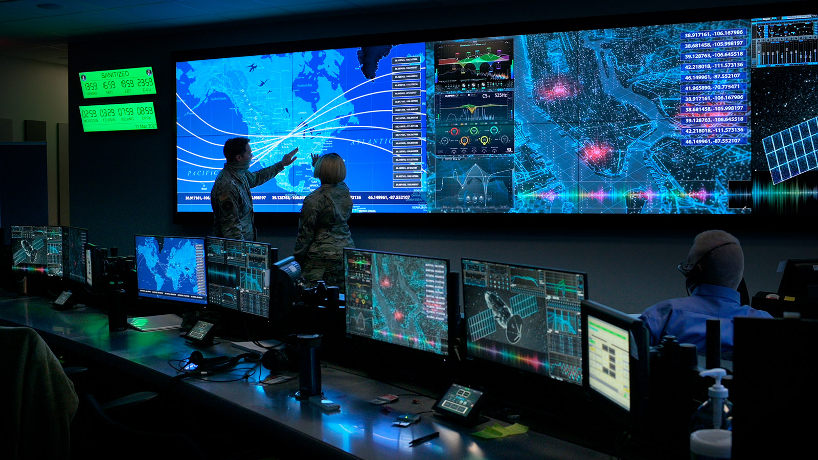 Two analysts in military uniform point to a large digital map displaying global tracking lines and data visualizations in a dark, high-tech command center.