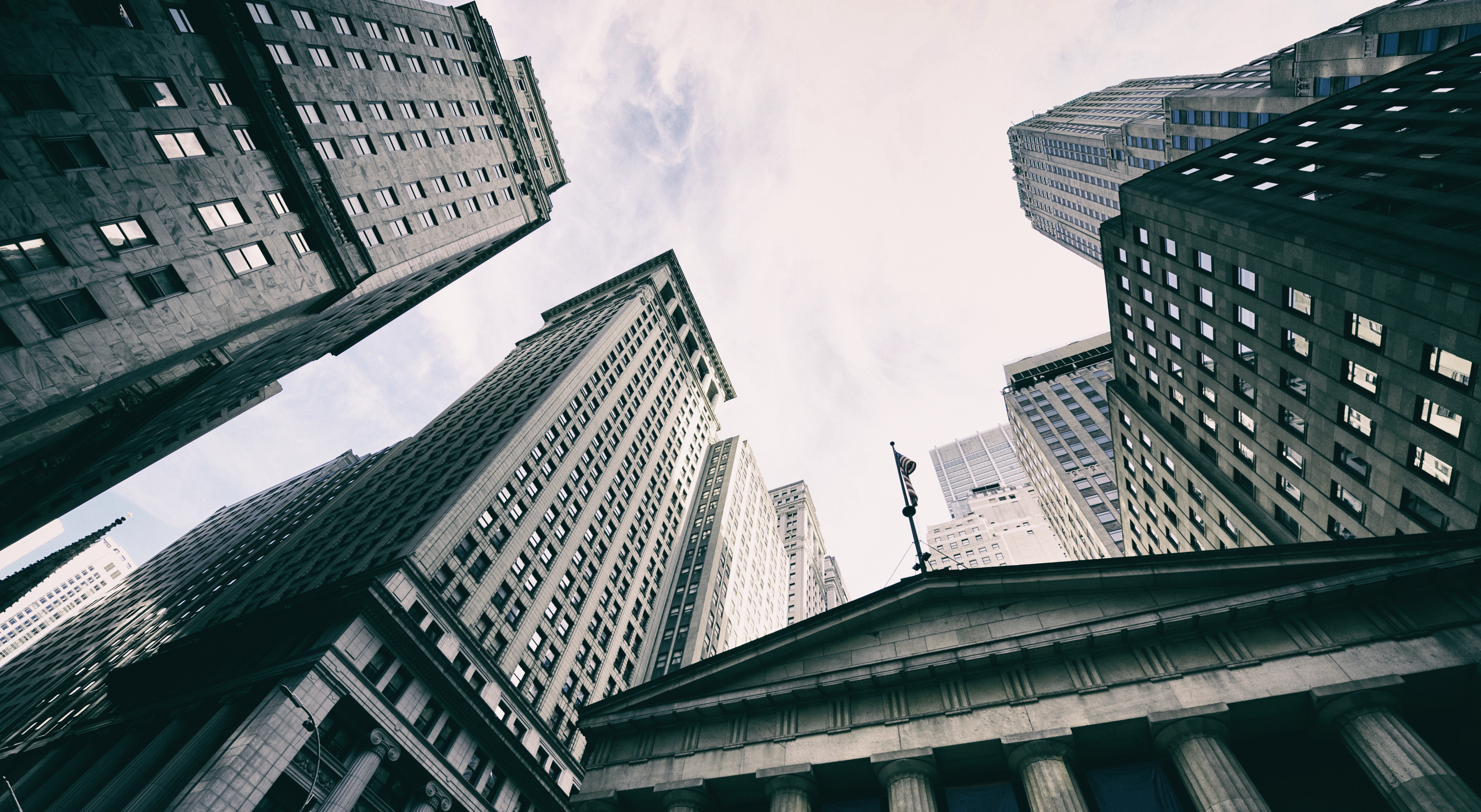 View looking up at tall city buildings and skyscrapers against a cloudy sky.
