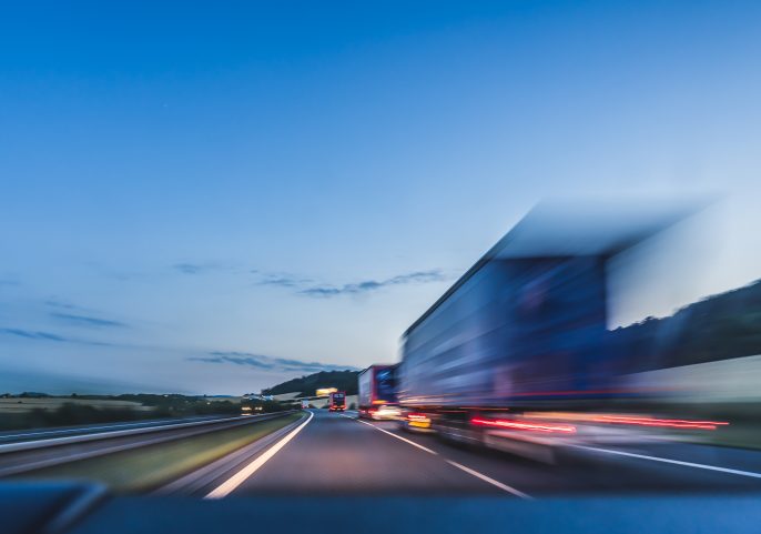 Blurred motion of a truck speeding down a highway at dusk under a blue sky.