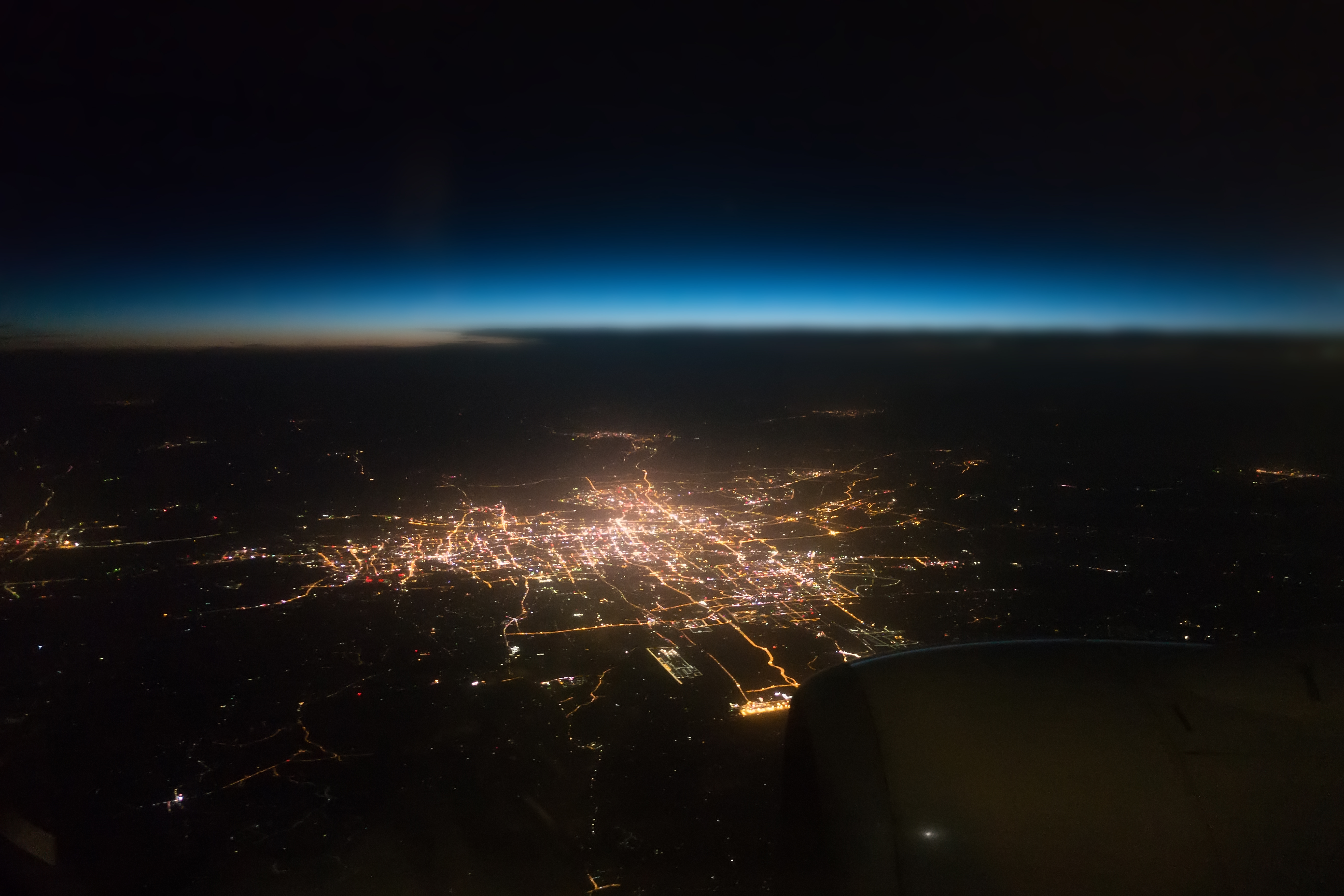 Aerial view of a brightly lit city sprawling out across the land at night, taken from a high altitude.