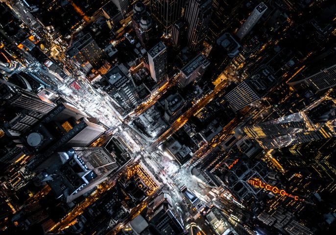 A dizzying aerial perspective looking straight down onto a busy metropolitan area at night, highlighting the grid of streets and buildings.