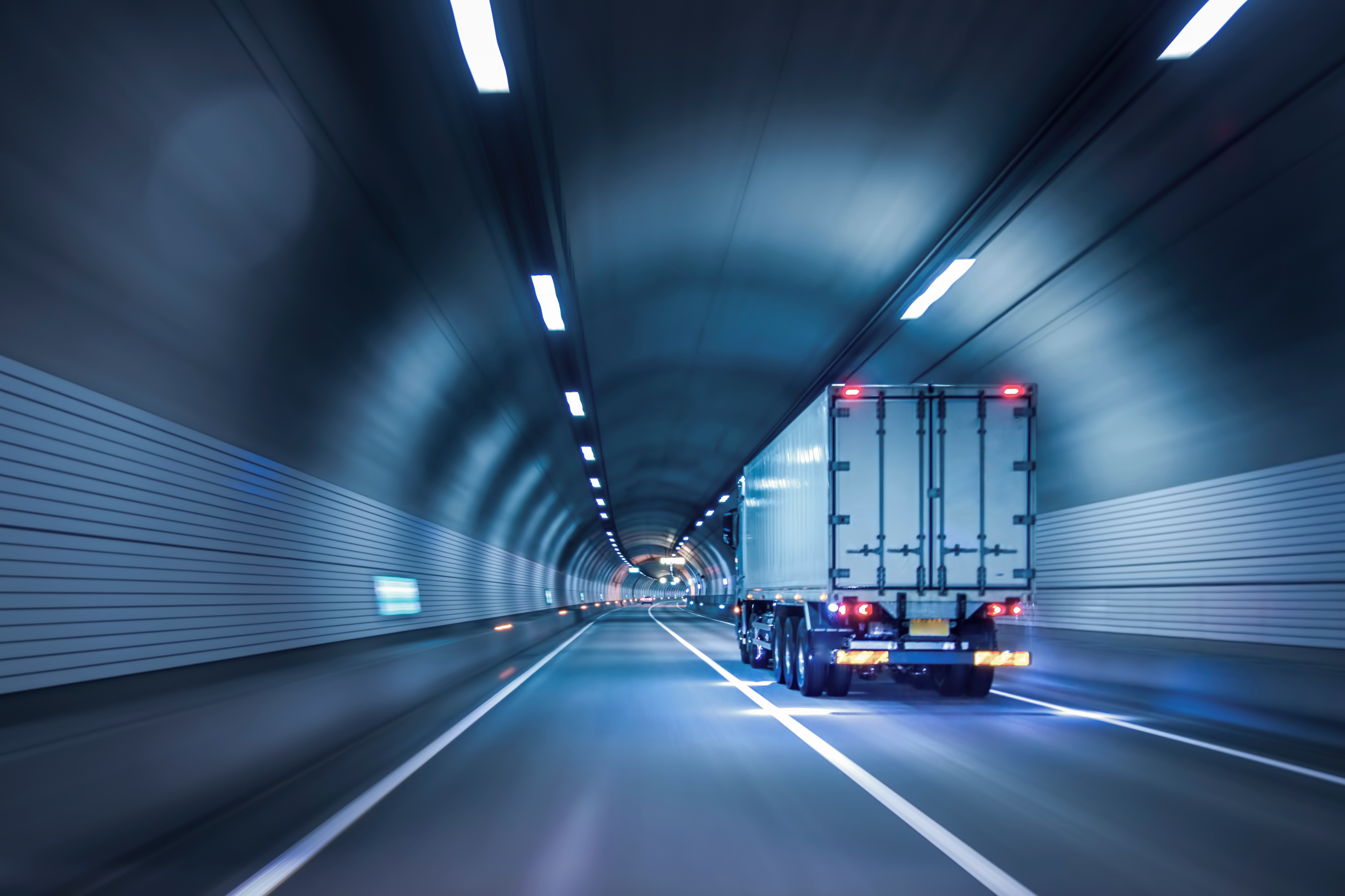 Rear view of a semi-truck driving through a brightly lit, long, modern highway tunnel.