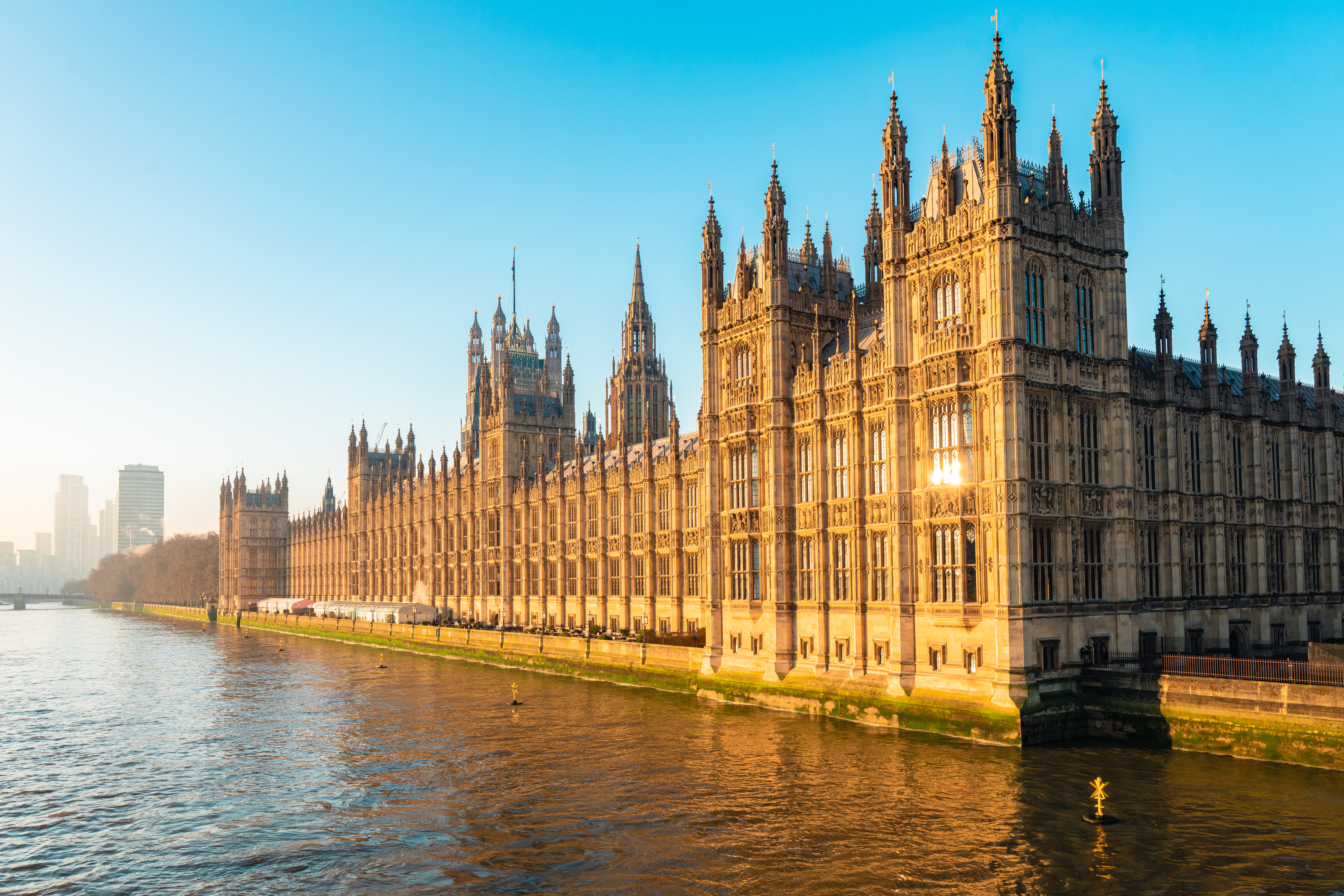 The Palace of Westminster and Big Ben glow in golden sunlight beside the River Thames.