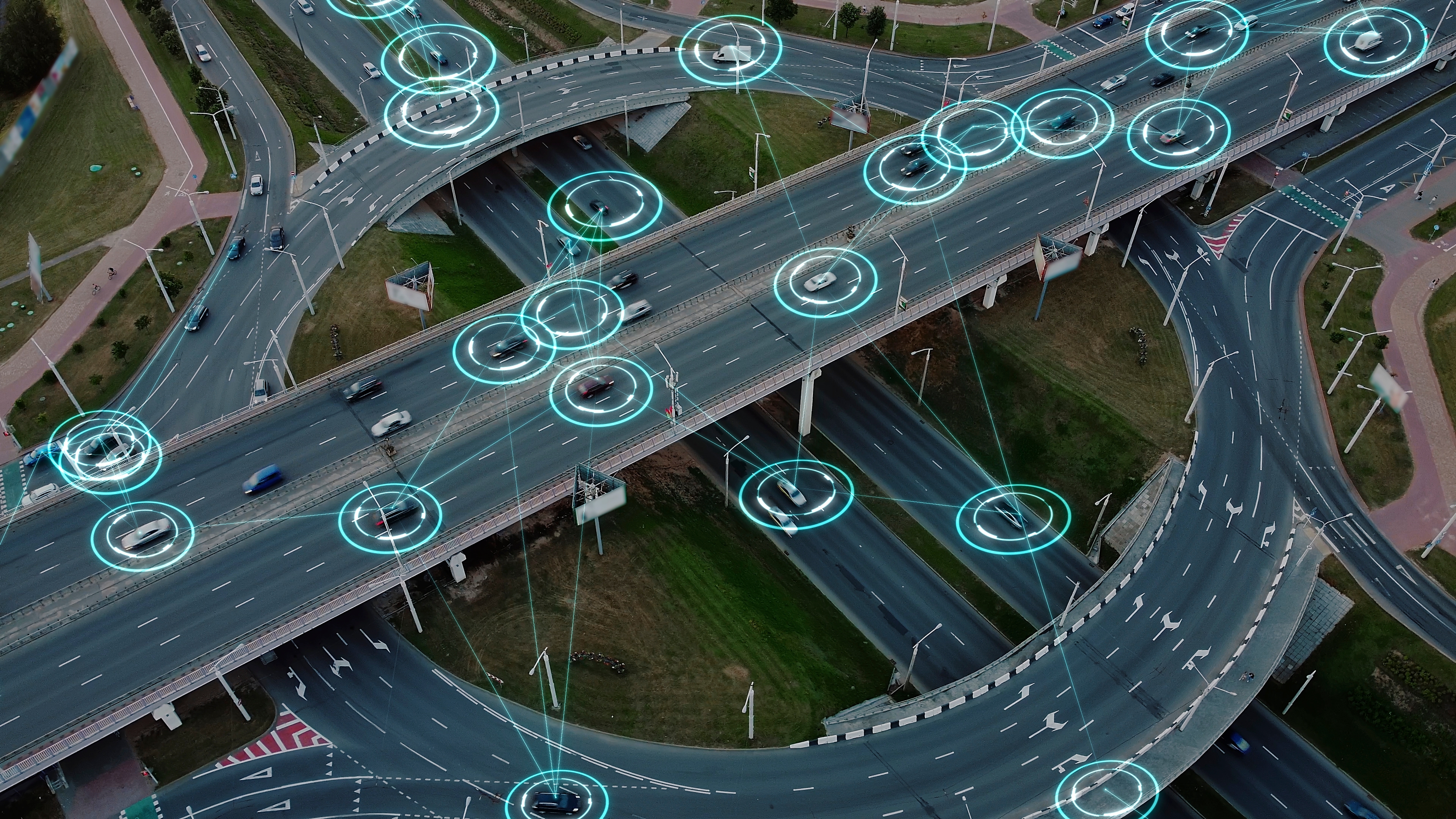Overhead shot of a road interchange with digital glowing circles tracking vehicles on the overpasses and ramps.
